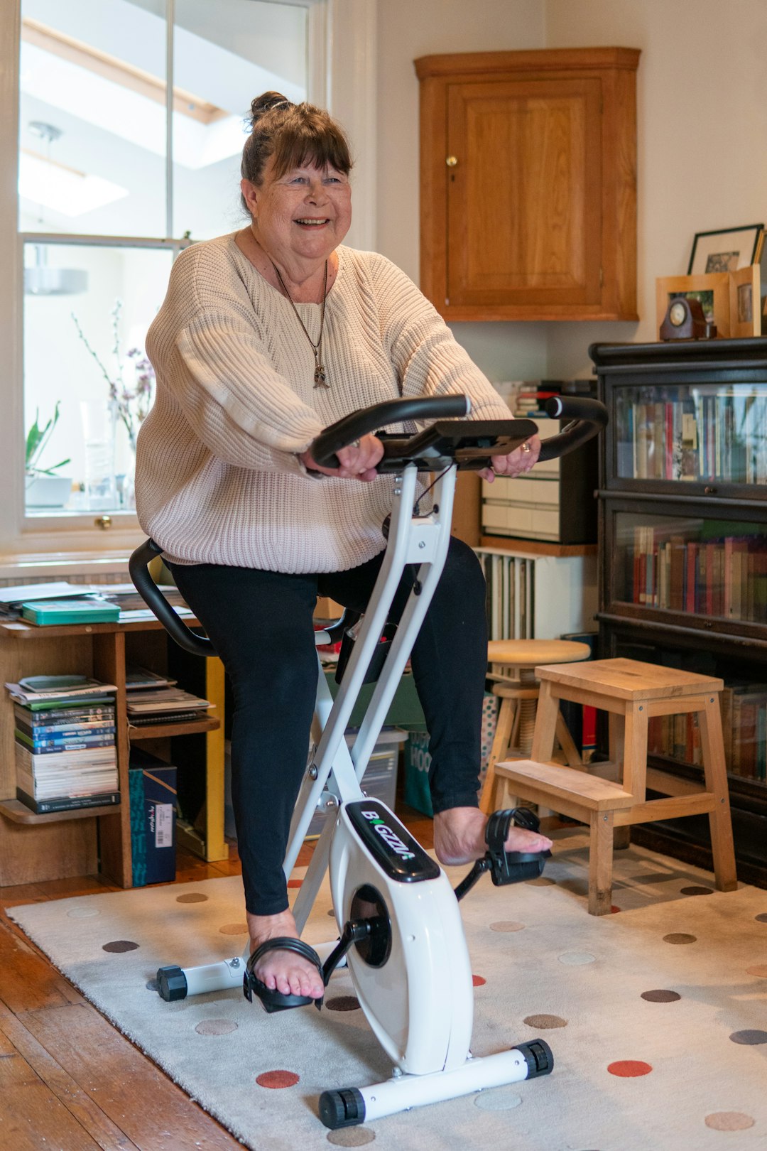 An older woman on an exercise bike at home.
